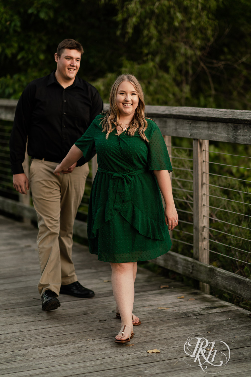 Man in black dress shirt walking with woman in green dress on a bridge in Eagan, Minnesota.