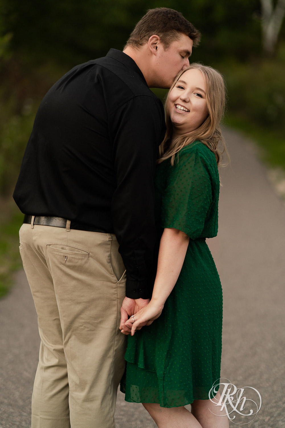 Man in black dress shirt kissing woman in green dress on foot path in Eagan, Minnesota.