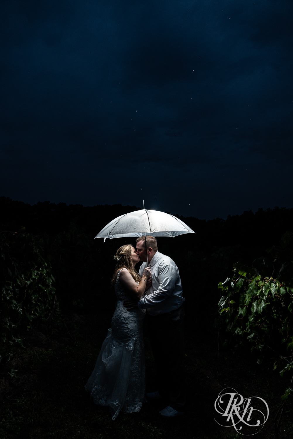 Bride and groom kissing under umbrella on rainy wedding night at 7 Vines Vineyard in Dellwood, Minnesota.