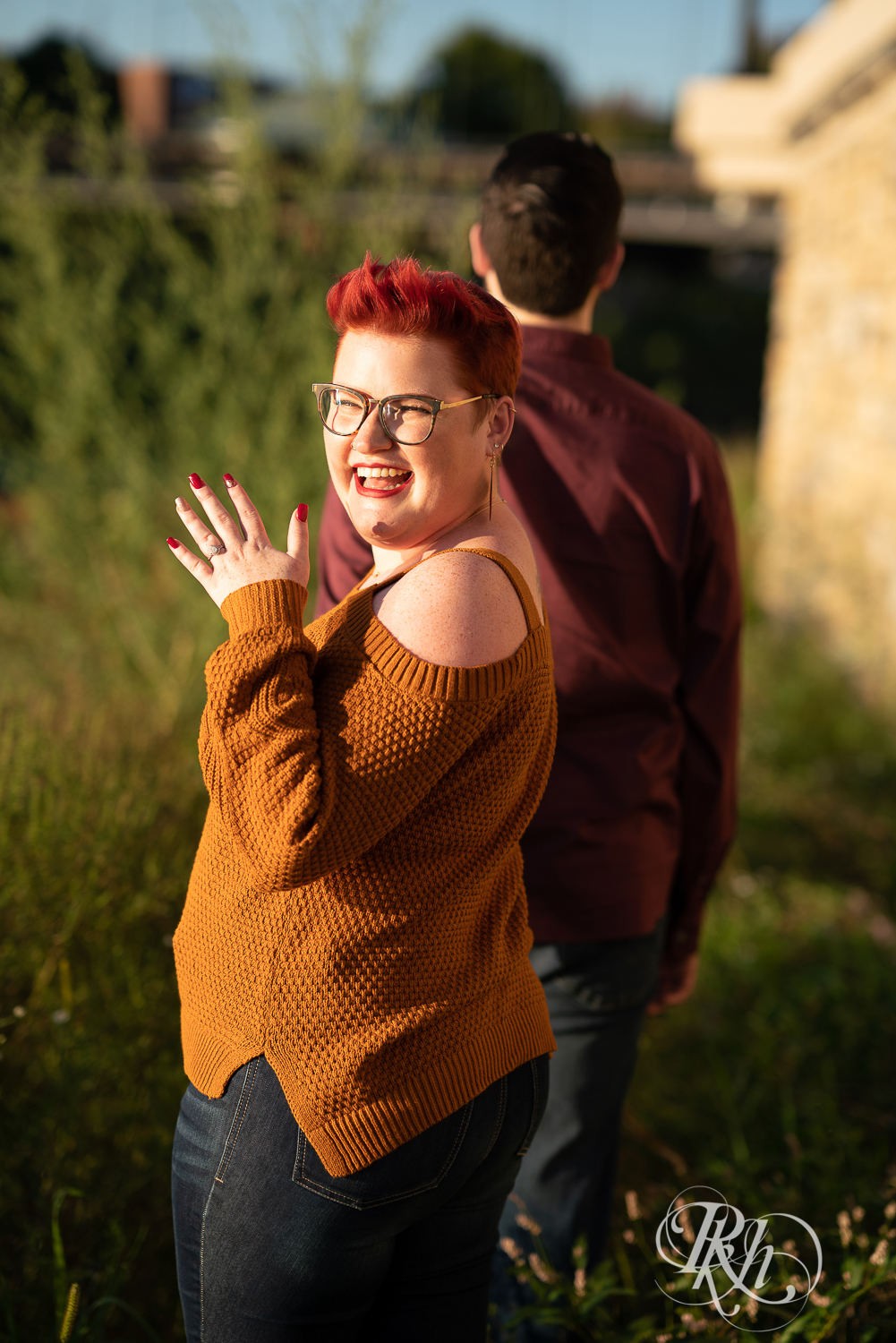 Man and woman with glasses and pixie red hair showing off engagement ring in Phoenix Park in Eau Claire, Wisconsin.