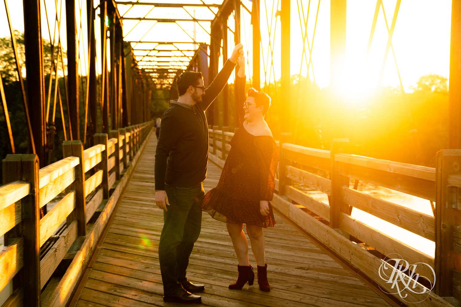 Man and woman with glasses and pixie red hair dancing on bridge at sunset in Phoenix Park in Eau Claire, Wisconsin.