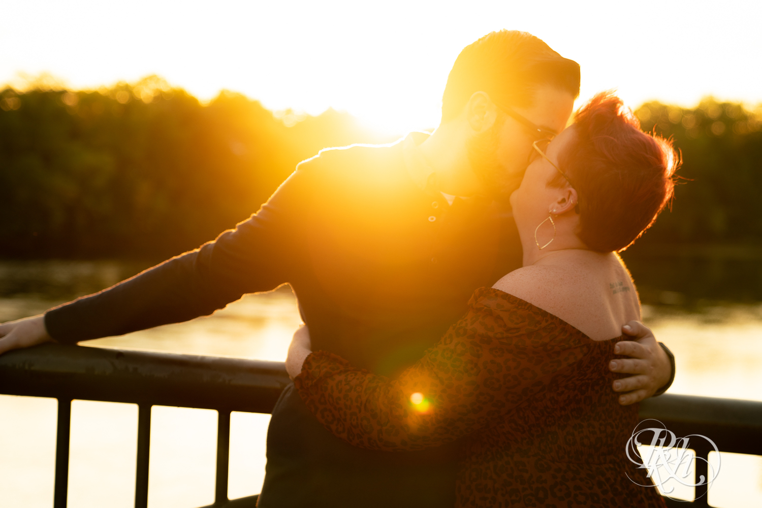 Man and woman with glasses and pixie red hair kissing on bridge at sunset in Phoenix Park in Eau Claire, Wisconsin.