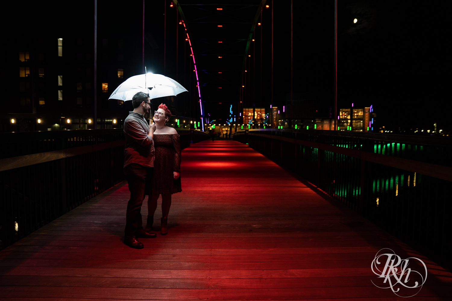Man and woman with glasses and pixie red hair under umbrella on bridge in Phoenix Park in Eau Claire, Wisconsin.