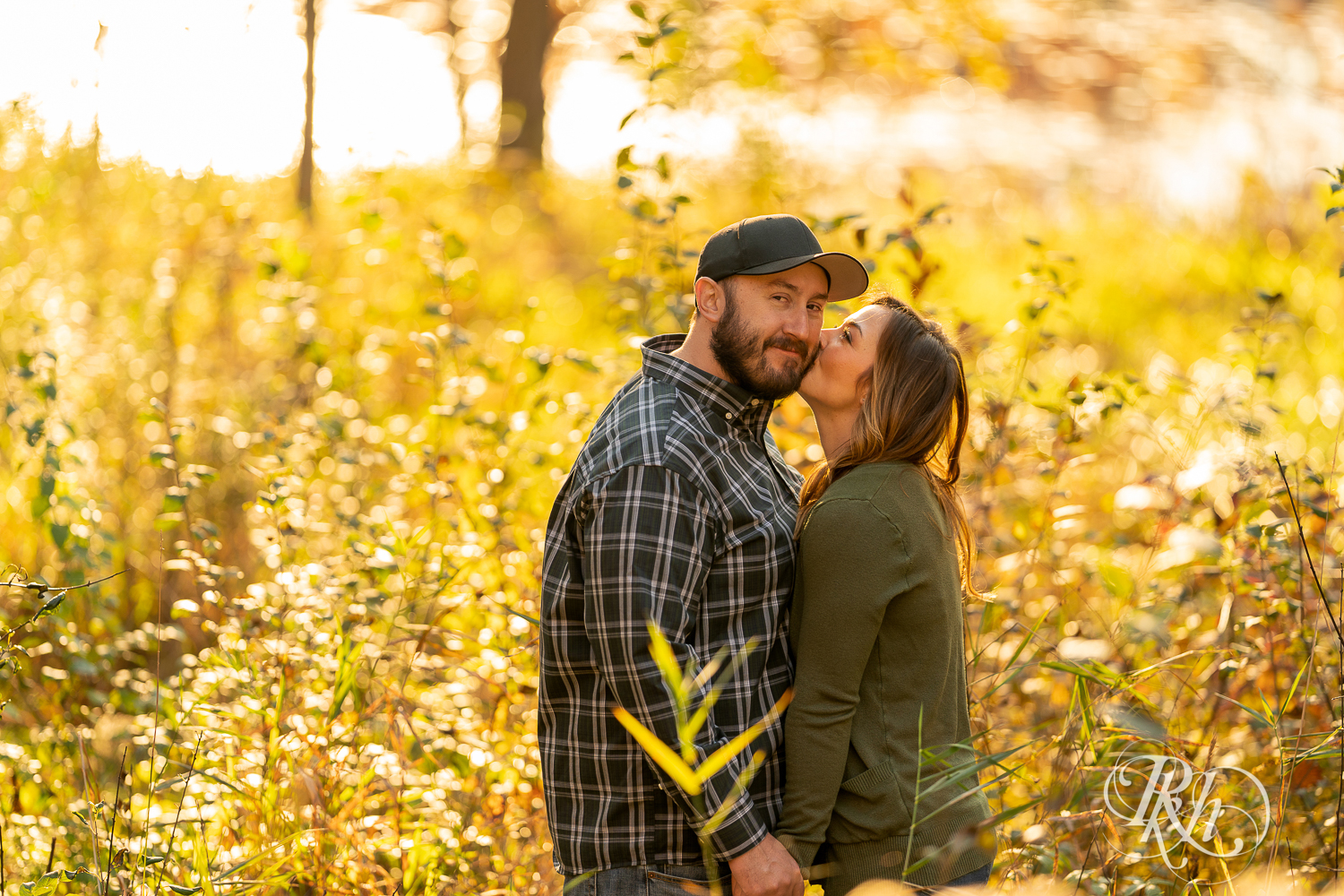 Man in flannel and woman in jeans and sweater kissing in field during sunset in Eagan, Minnesota.