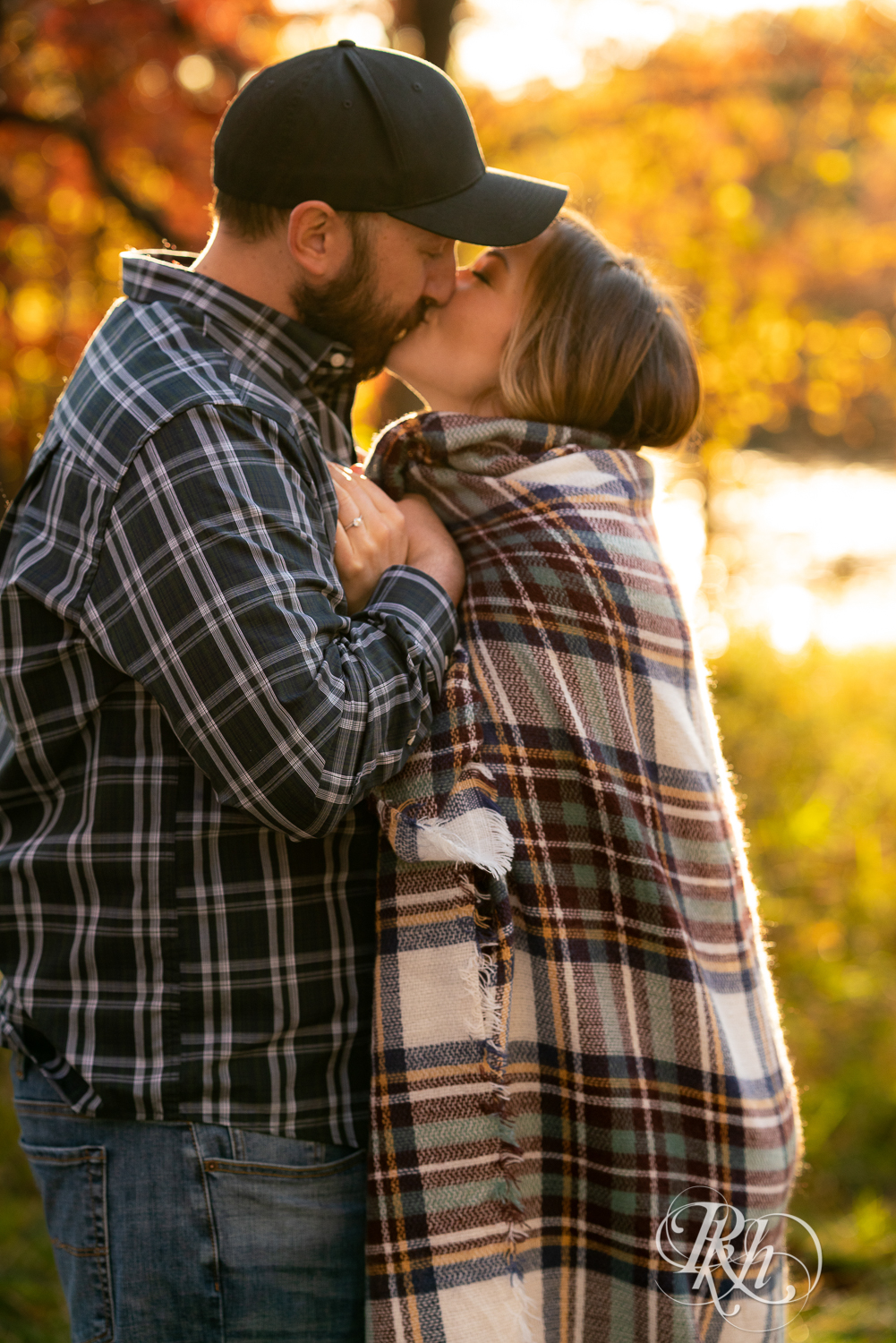 Man in flannel and woman in jeans and sweater kissing in field during sunset in Eagan, Minnesota.