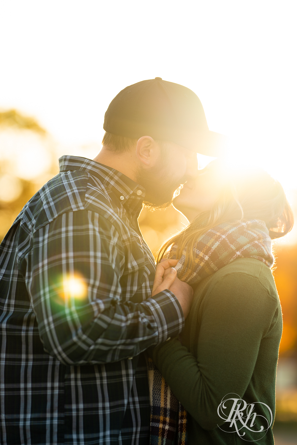 Man in flannel and woman in jeans and sweater kissing during sunset in Eagan, Minnesota.