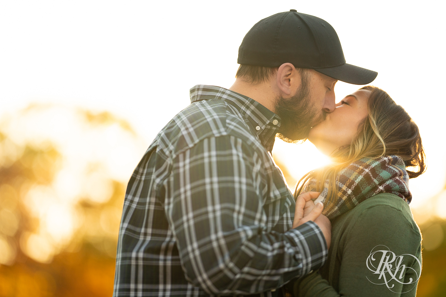 Man in flannel and woman in jeans and sweater kissing during sunset in Eagan, Minnesota.