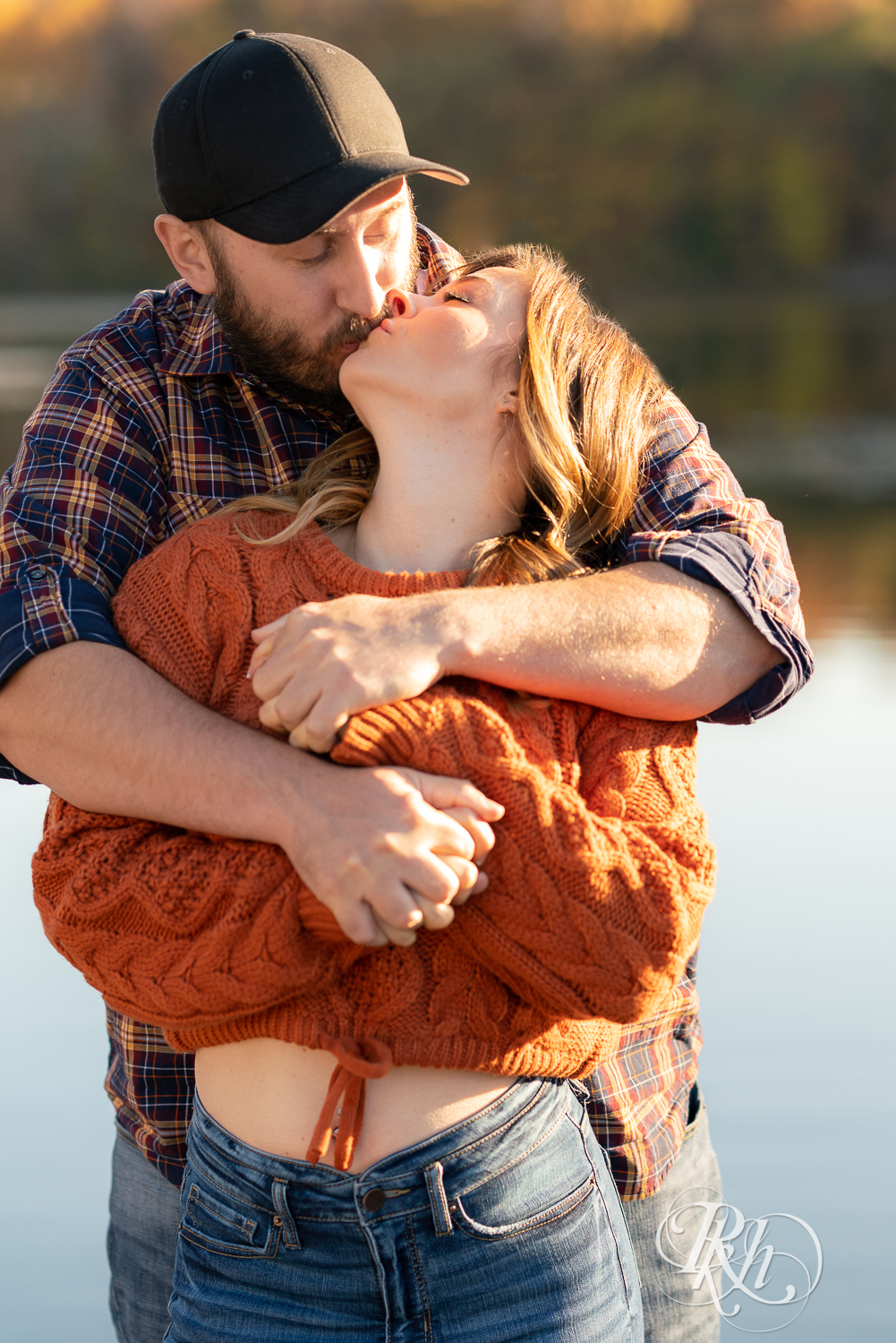 Man in flannel and woman in jeans and sweater kissing in sunset in Eagan, Minnesota.