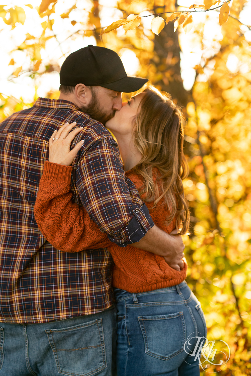 Man in flannel and woman in jeans and sweater kissing in sunset in Eagan, Minnesota.