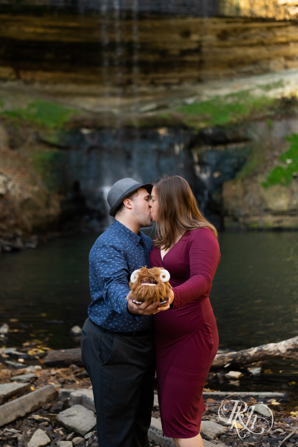 Man wearing hat kisses woman in red dress in Minnehaha Falls in Minneapolis, Minnesota, while holding stuffed Bantha.