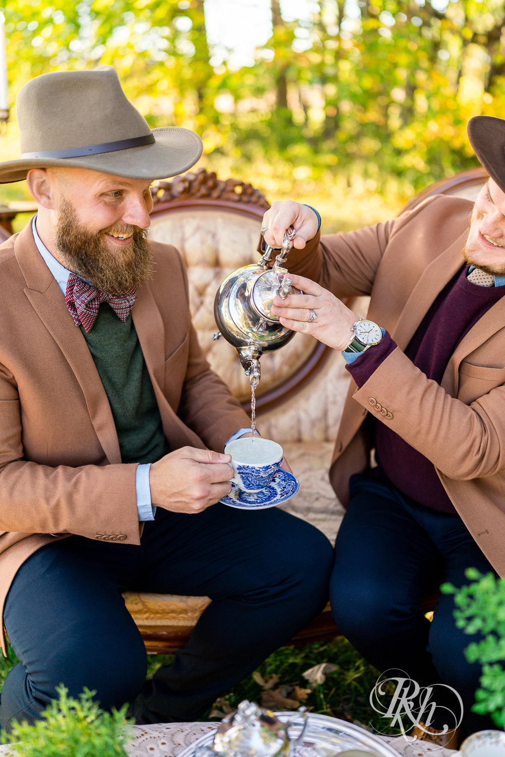 Two gay men smiling in suits and hats having tea in Belle Plaine, Minnesota.