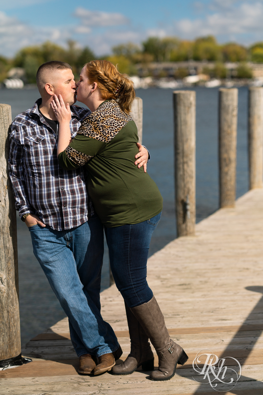 Man in flannel and jeans kisses woman in sweater and jeans on a dock in Excelsior, Minnesota.