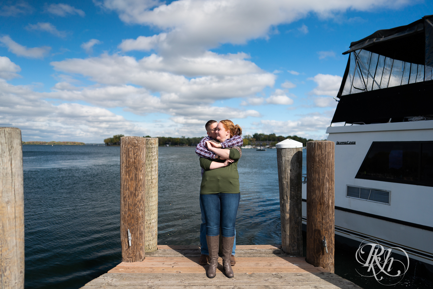 Man in flannel and jeans hugs woman in sweater and jeans on a dock in Excelsior, Minnesota.