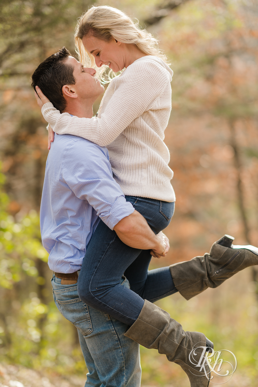Man lifting blonde woman in leaves during fall engagement photography session in Chaska, Minnesota.