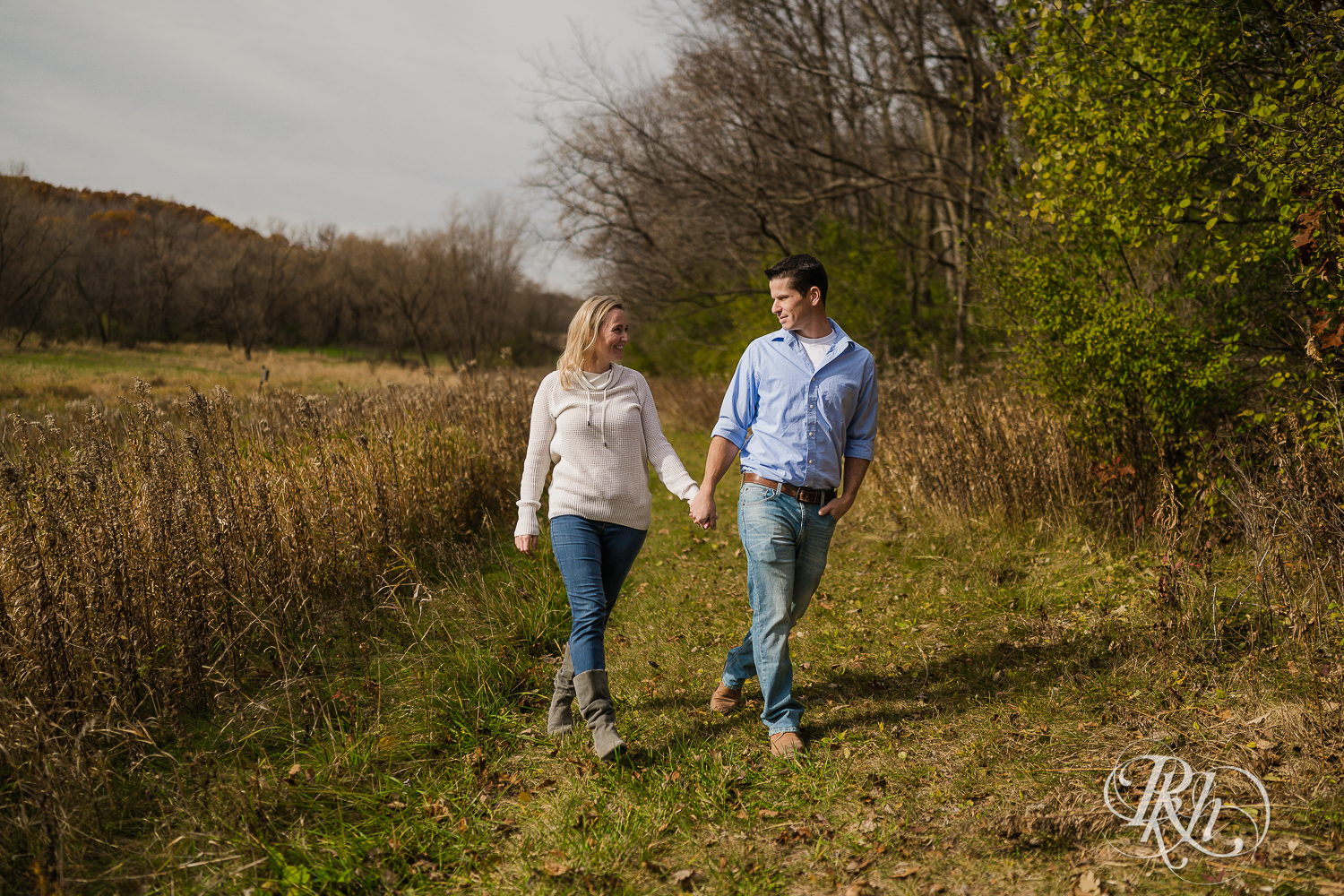 Man walking with blonde woman in grass during fall engagement photography session in Chaska, Minnesota.