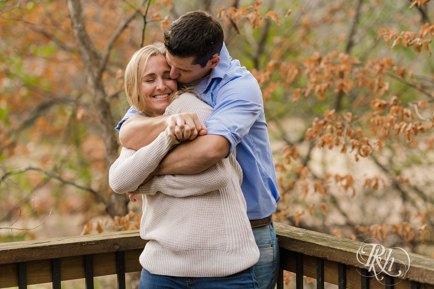 Man kisses blonde woman in leaves during fall engagement photography session in Chaska, Minnesota.