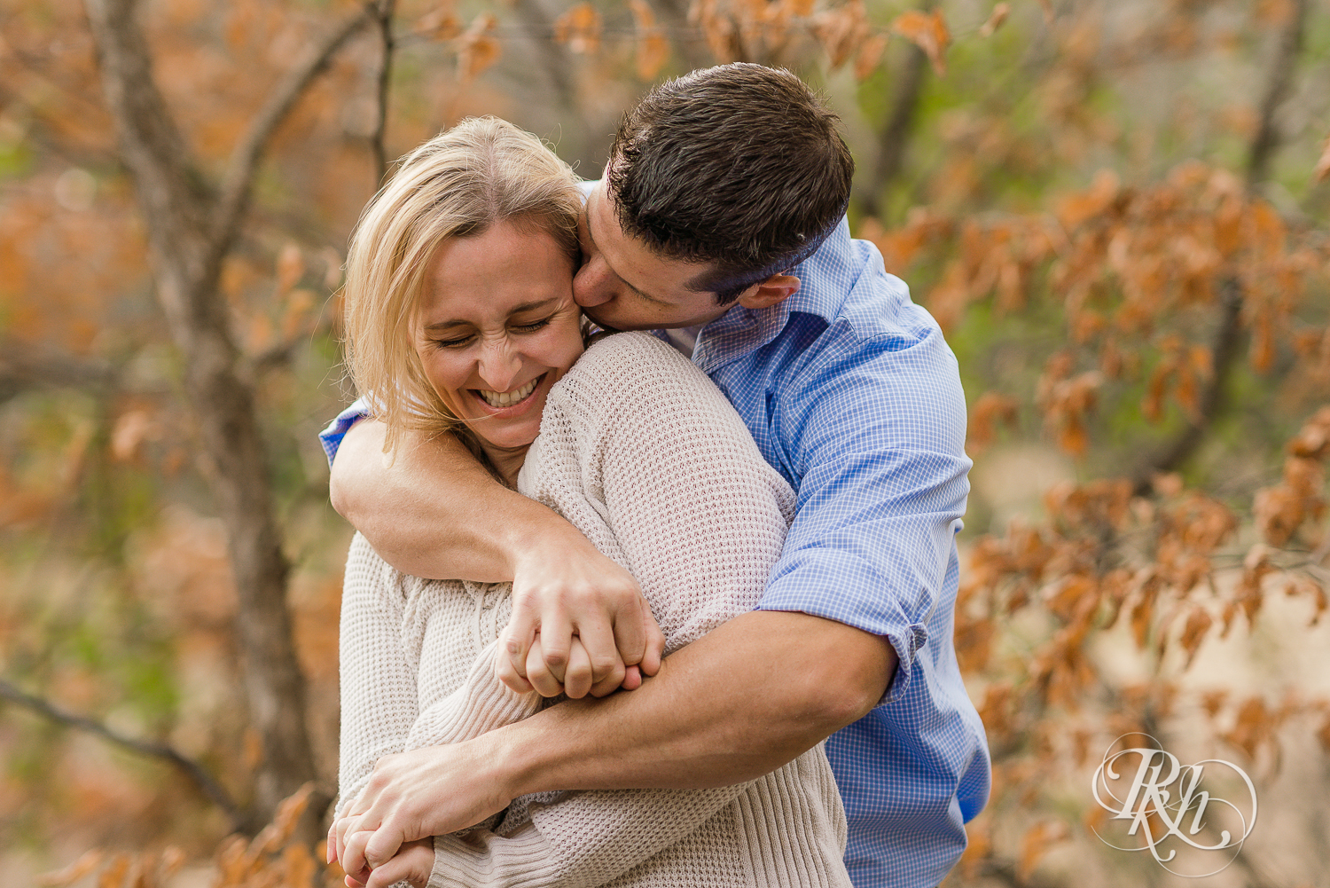 Man kisses blonde woman in leaves during fall engagement photography session in Chaska, Minnesota.