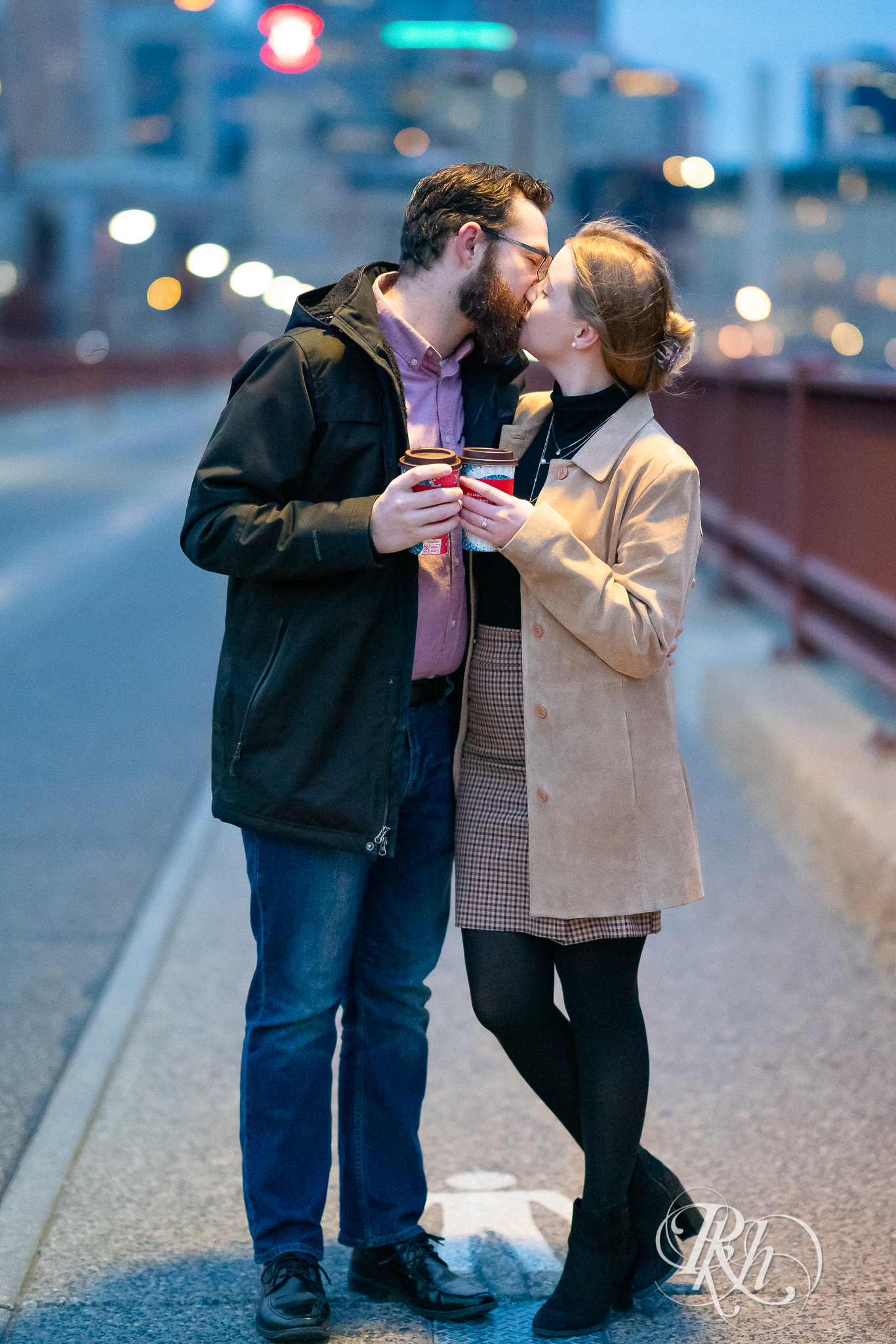 Man and woman kissing and holding coffee cups on the Stone Arch Bridge in Minneapolis, Minnesota at sunrise.
