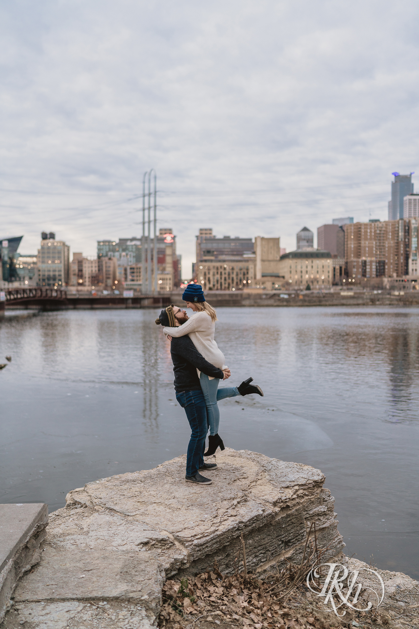 Man lifting and kissing woman in front of Mississippi River in Minneapolis, Minnesota at sunrise. 