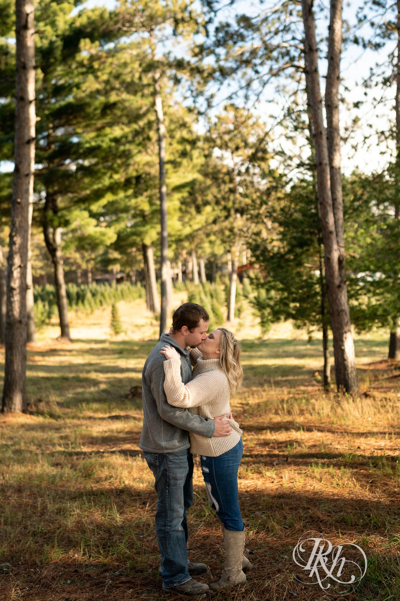 Man and woman kissing in between trees at Hansen Tree Farm in Anoka, Minnesota.