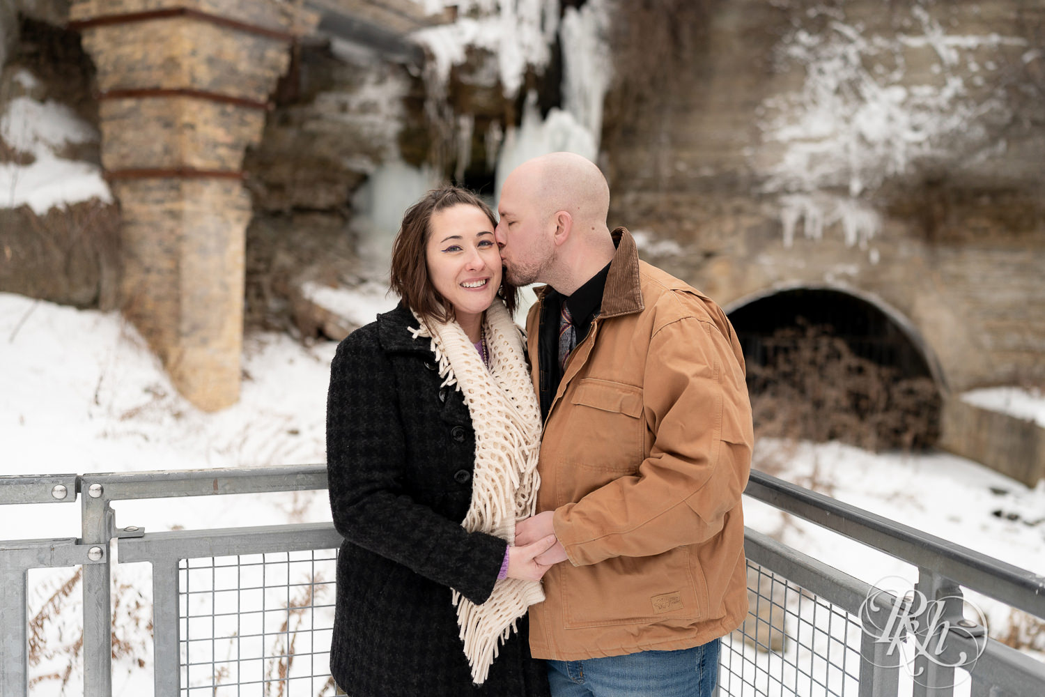 Man and woman standing in front of frozen waterfall in snow at Mill City Ruins in Minneapolis, Minnesota.