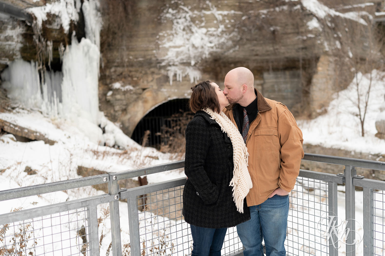 Man and woman kissing in front of frozen waterfall in snow at Mill City Ruins in Minneapolis, Minnesota.