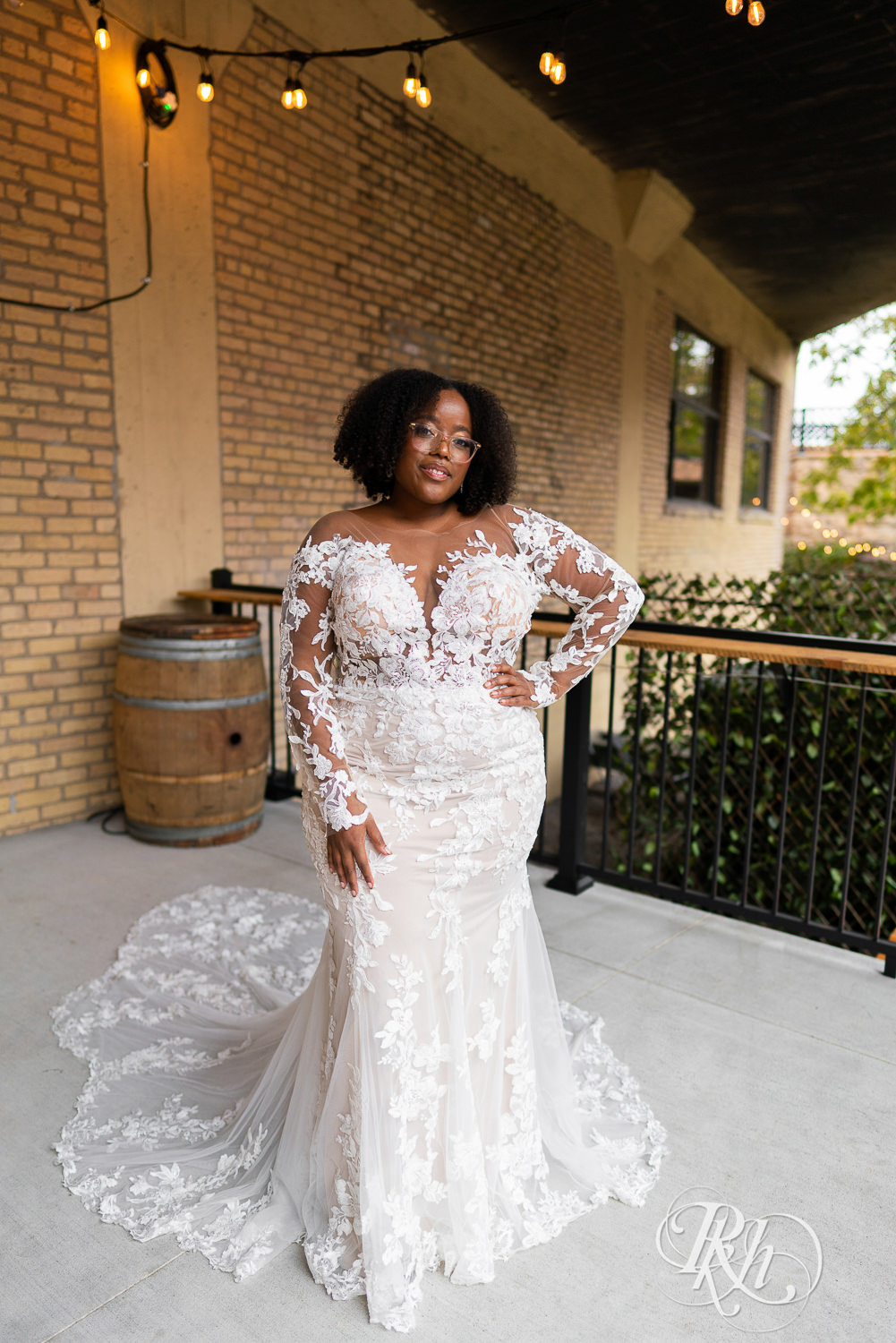 Black plus size bride in glasses smiling in wedding dresses in Minneapolis, Minnesota with hand on hip.