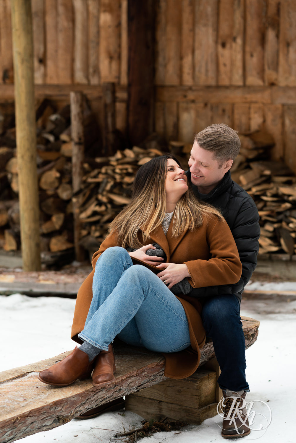Man and woman sitting in front of woodpile in the snow at Hansen Tree Farm in Anoka, Minnesota.