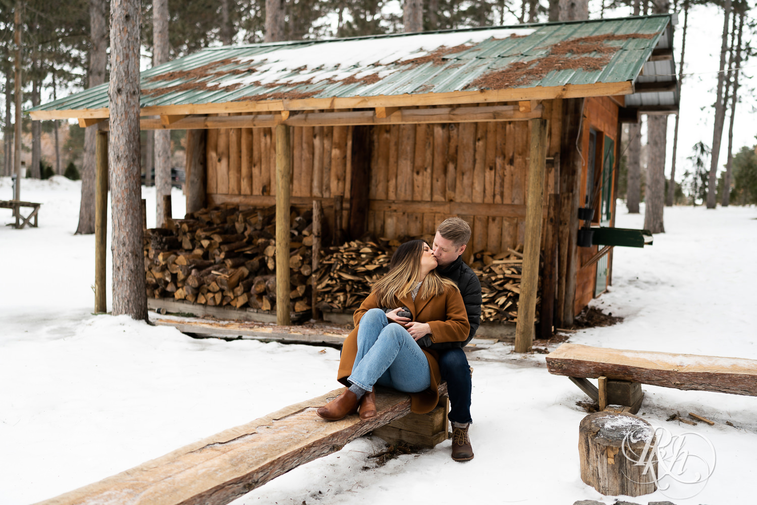 Man and woman sitting in front of woodpile in the snow at Hansen Tree Farm in Anoka, Minnesota.