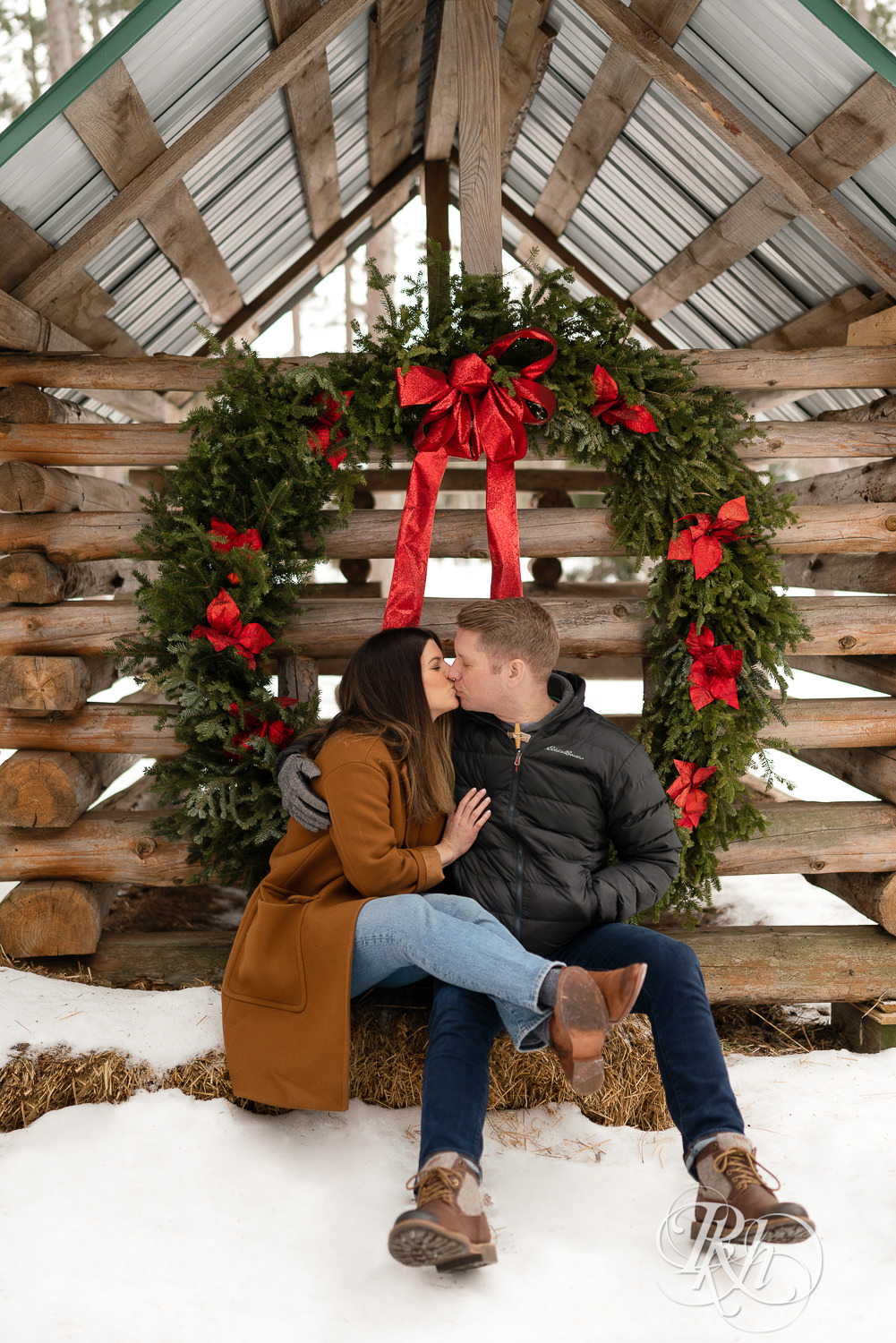 Man and woman kissing in front of Christmas wreath in the snow at Hansen Tree Farm in Anoka, Minnesota.