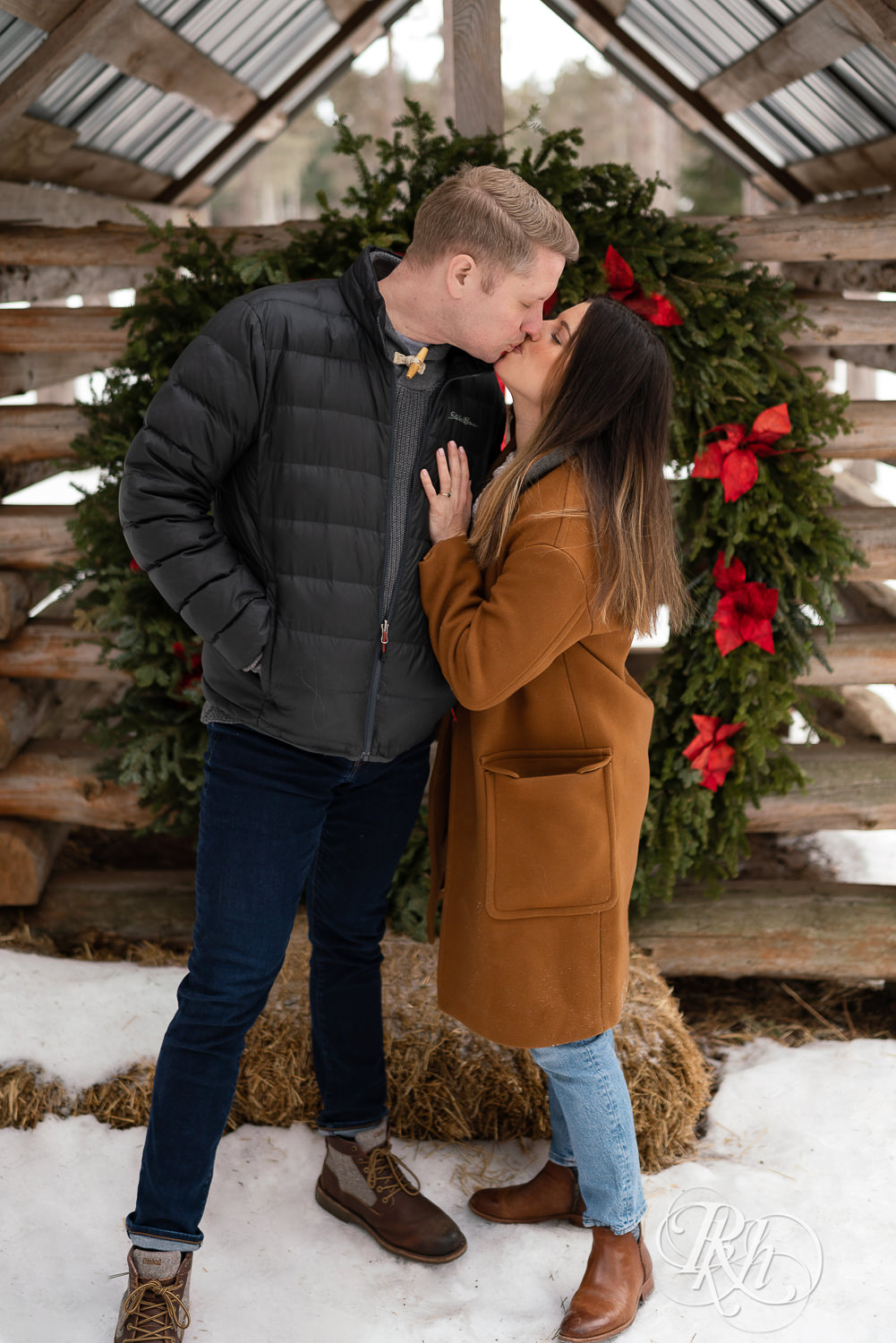 Man and woman kissing in front of Christmas wreath in the snow at Hansen Tree Farm in Anoka, Minnesota.