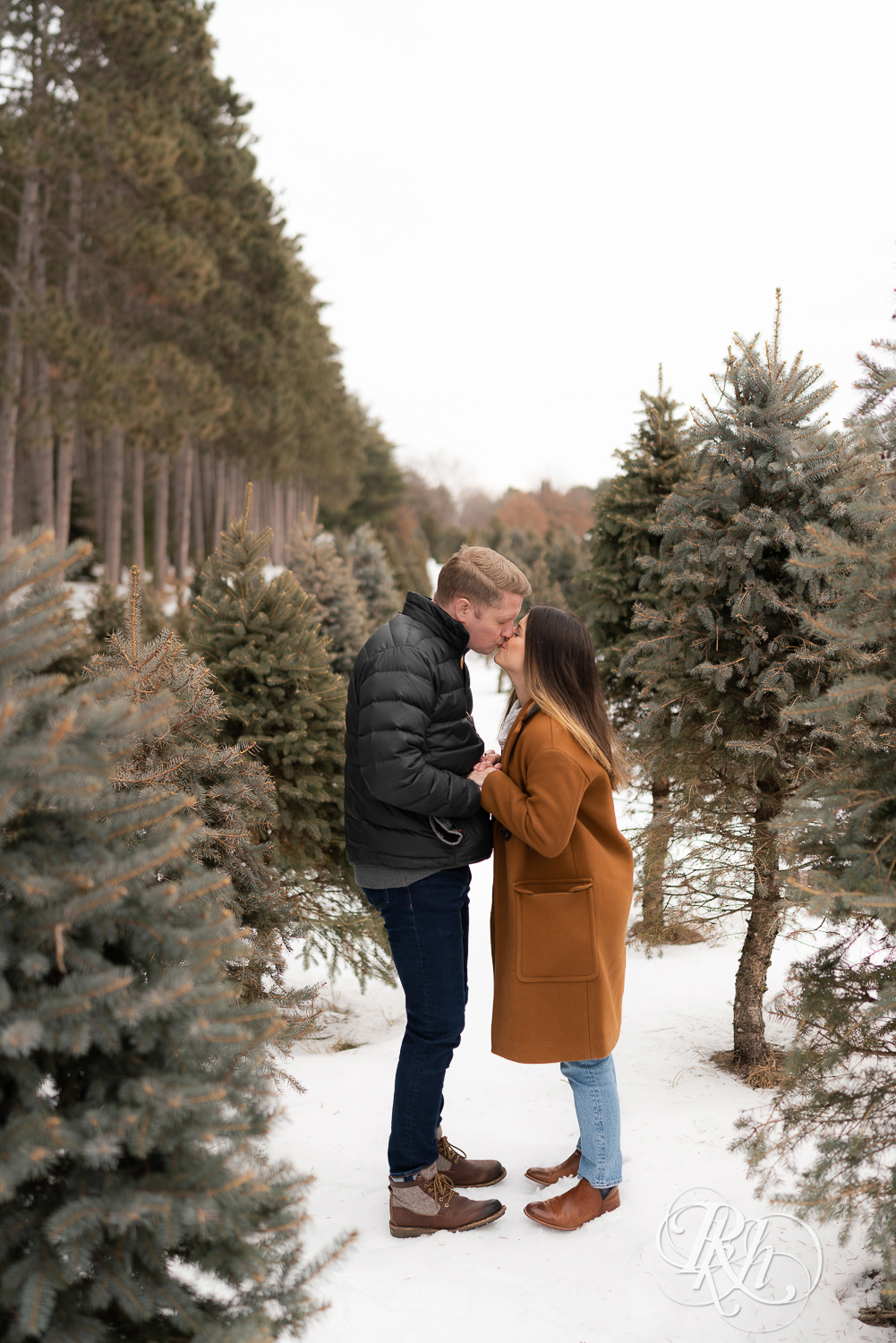 Man and woman kissing in between pine trees in the snow at Hansen Tree Farm in Anoka, Minnesota.
