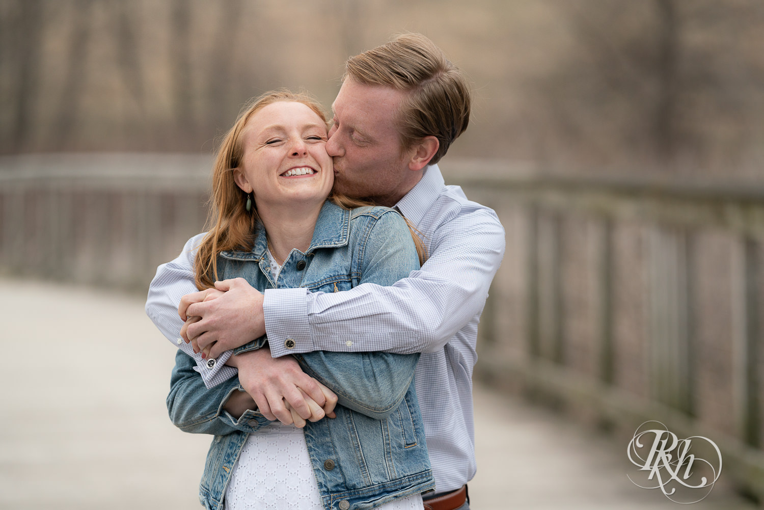 Redhead couple in denim smile and hug on bridge on cloudy day in Eagan, Minnesota.