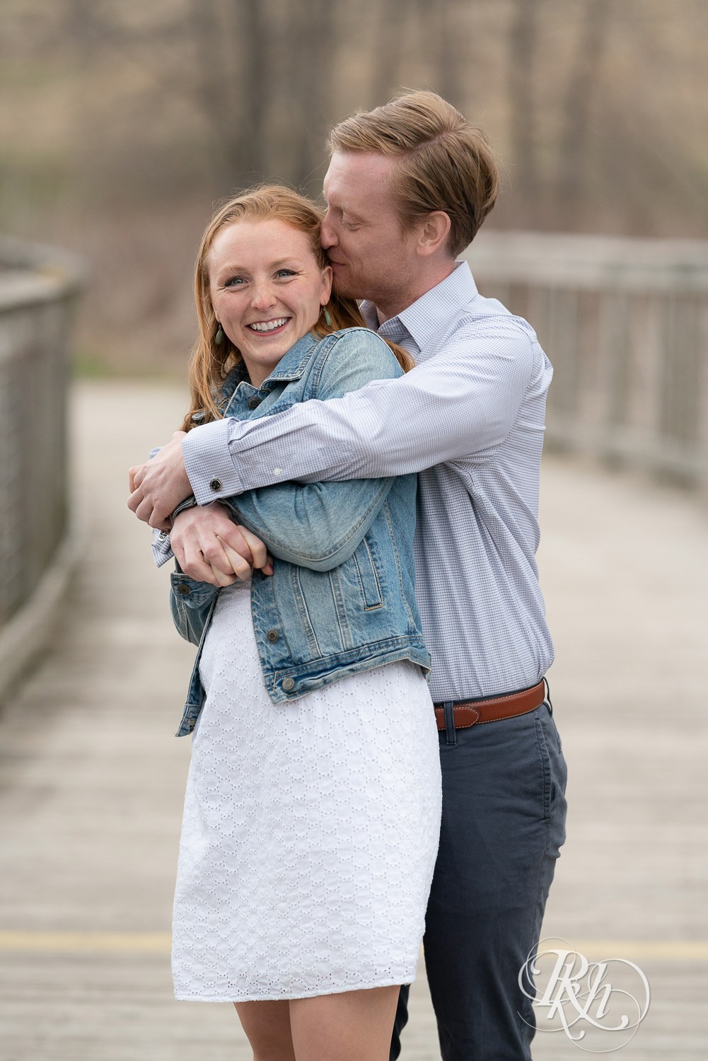 Redhead couple in denim smile and hug on bridge on cloudy day in Eagan, Minnesota.
