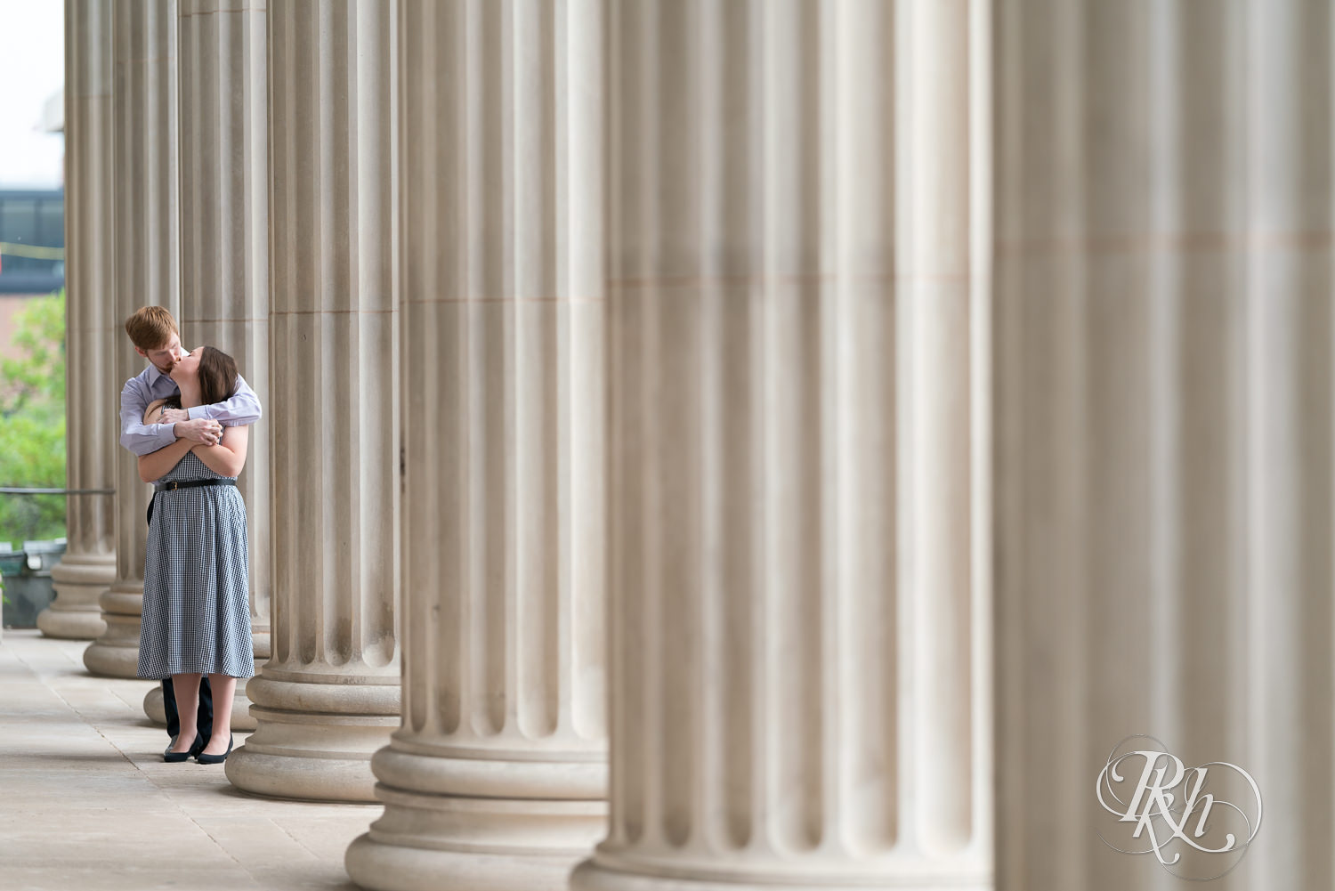 Man and woman kissing between columns during engagement session at University of Minnesota.