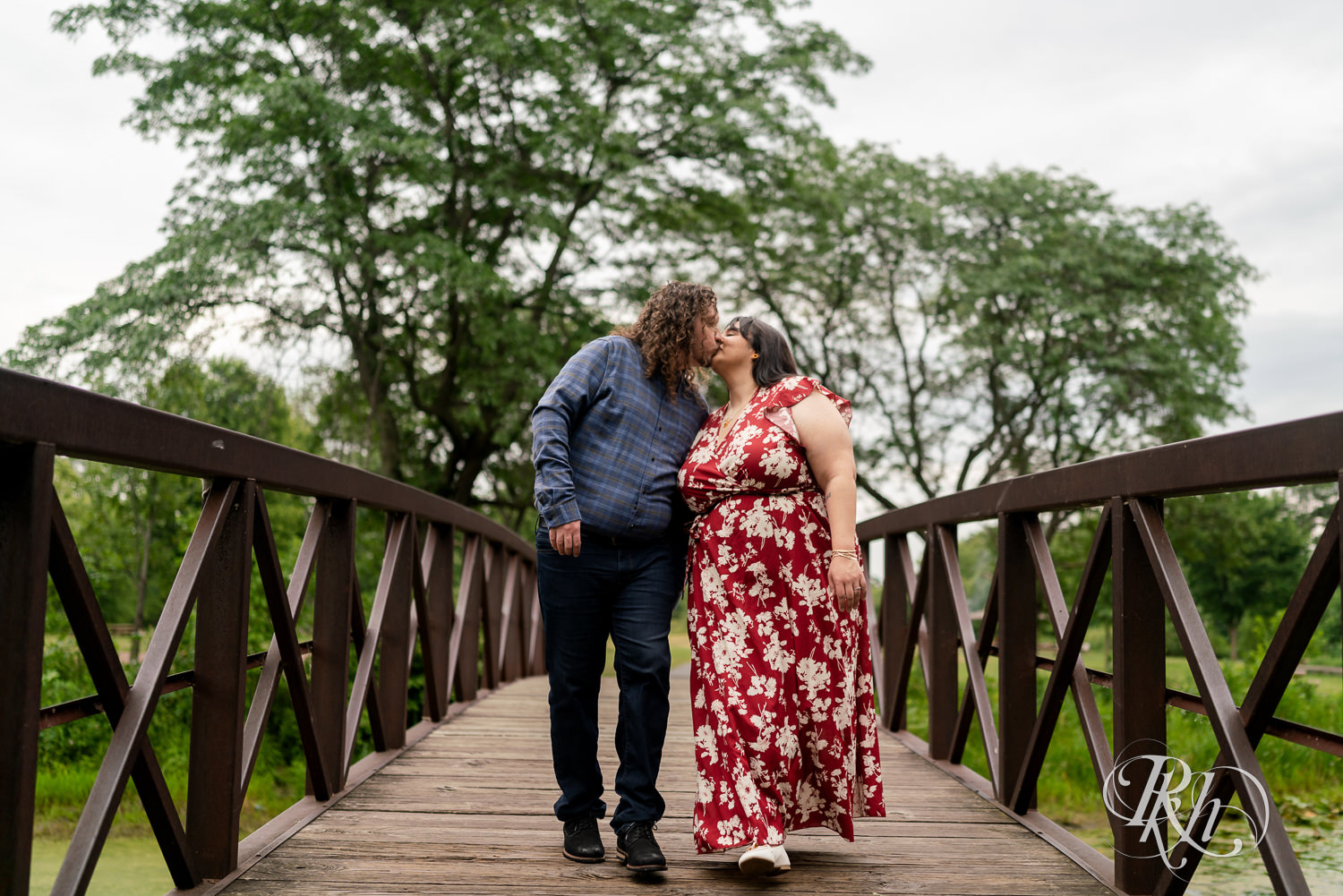 Man and woman in red dress kissing on bridge in Lake Phalen, Minnesota during engagement photography.