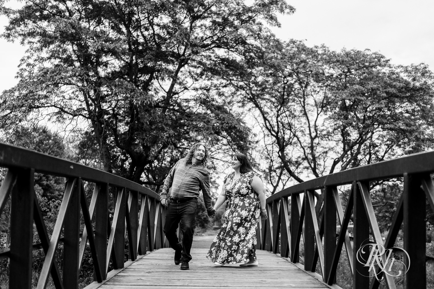 Man and woman in red dress walking across bridge in Lake Phalen, Minnesota during engagement photography.
