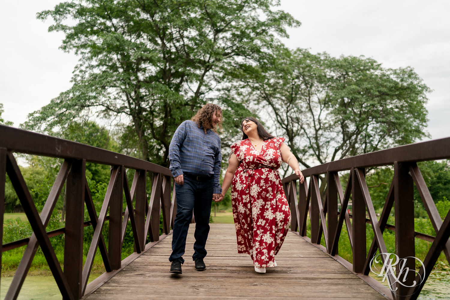 Man and woman in red dress walking across bridge in Lake Phalen, Minnesota during engagement photography.