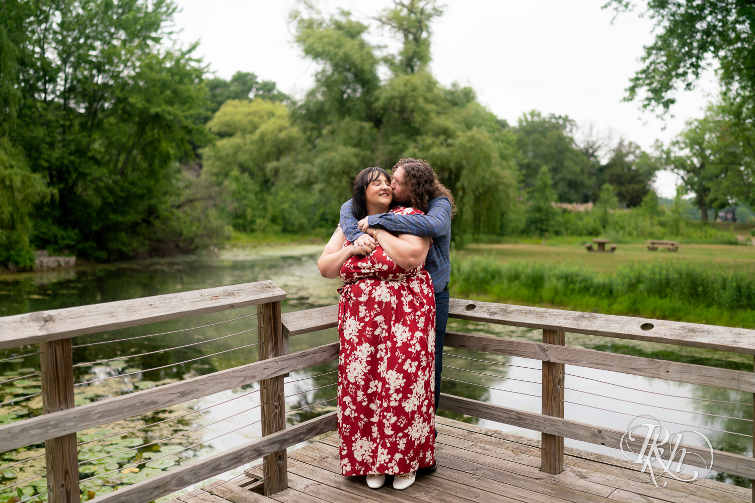 Man and woman in red dress hugging one another in Lake Phalen, Minnesota during engagement photography.