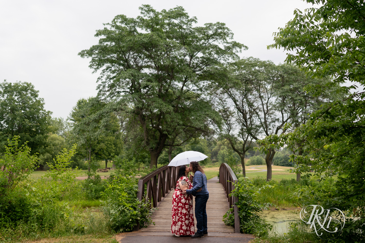 Man and woman holding umbrella in rainy Lake Phalen engagement photography