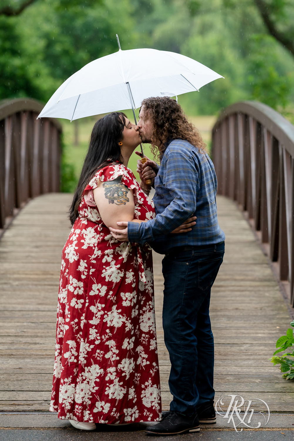 Man and woman holding umbrella in rainy Lake Phalen engagement photography