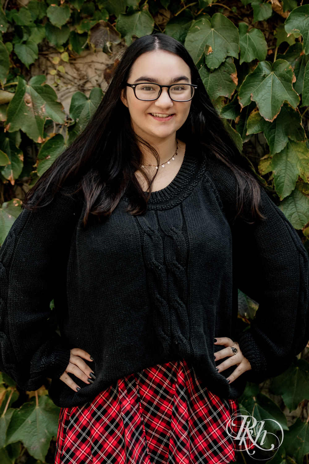 Girl dressed in glasses, sweater, and skirt looks at camera for senior photography in Mill City, Minneapolis.