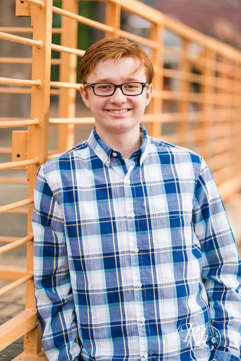 Redheaded boy in glasses and flannel looks at camera for senior pictures in Minneapolis.