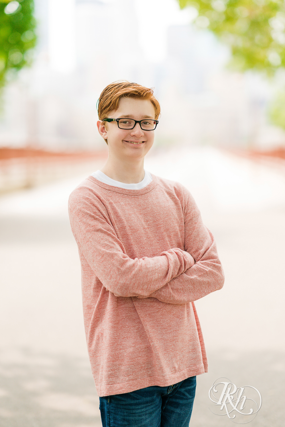 Redheaded boy in glasses and sweater looks at camera for senior pictures in Minneapolis.