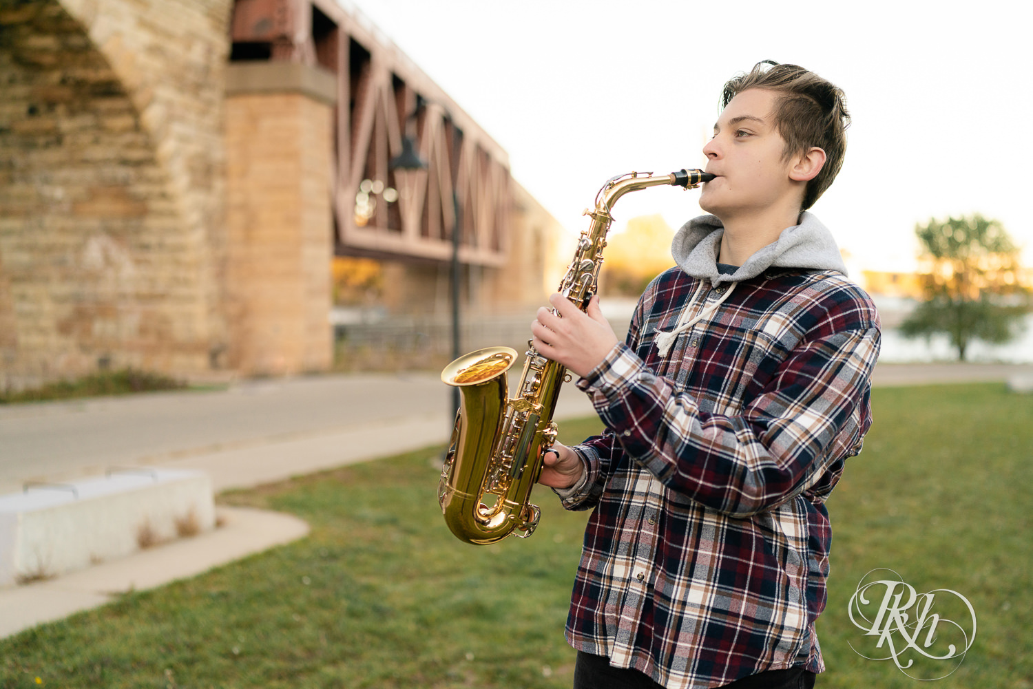 Senior boy dressed in flannel playing saxophone in Mill City Ruins in Minneapolis, Minnesota for senior photography