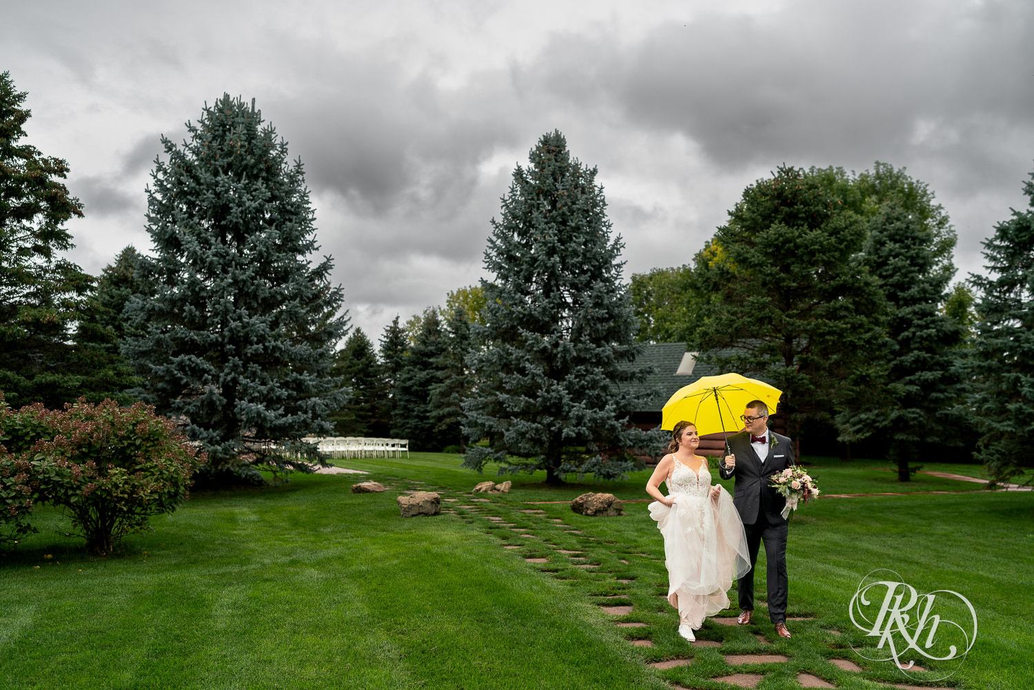Bride and groom walking under yellow umbrella on rainy day at Glenhaven Events in Farmington, Minnesota.