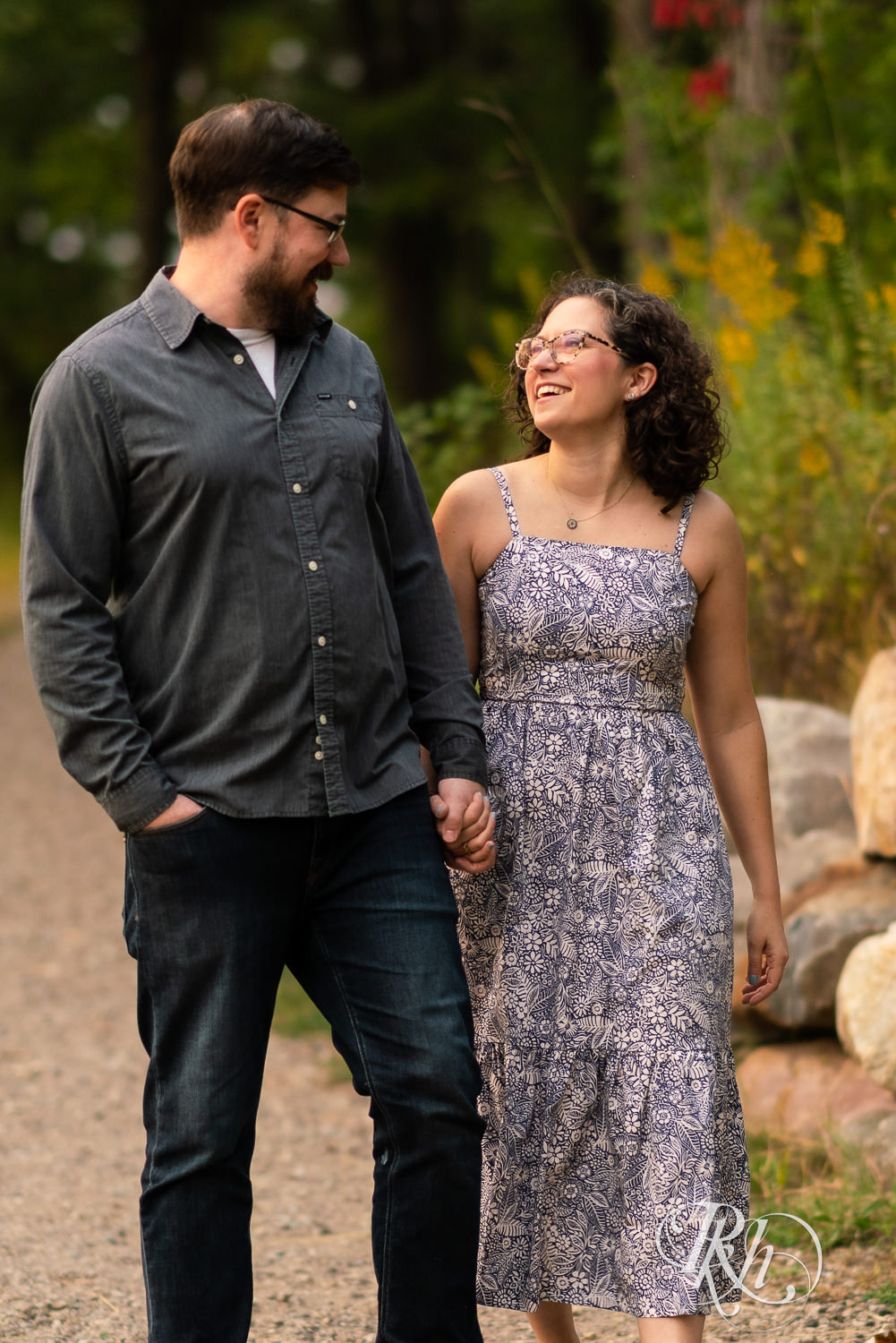 Man and woman in glasses laughing and walking at sunset engagement session.