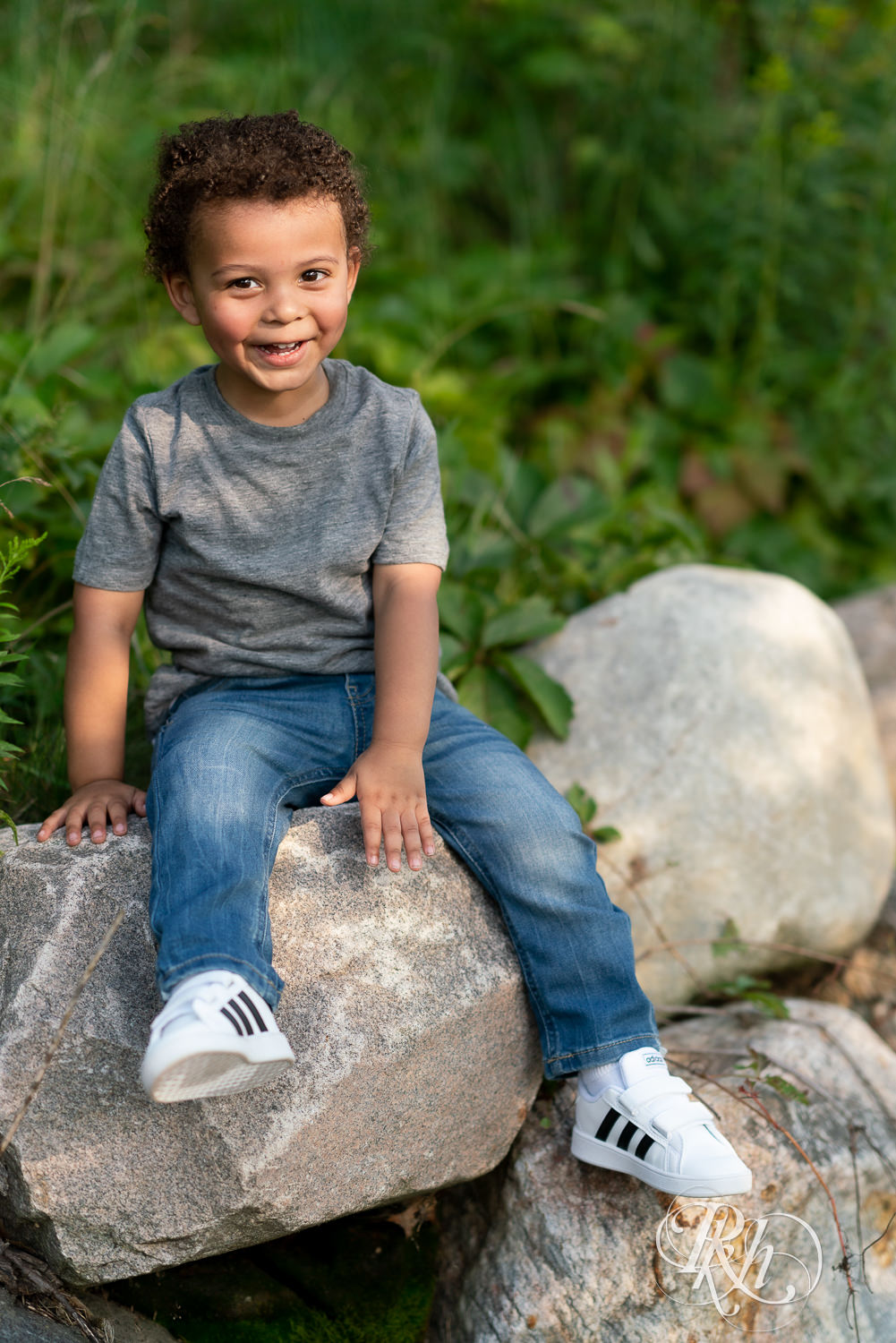 Little boy dressed in jeans and a gray shirt sitting on a rock.