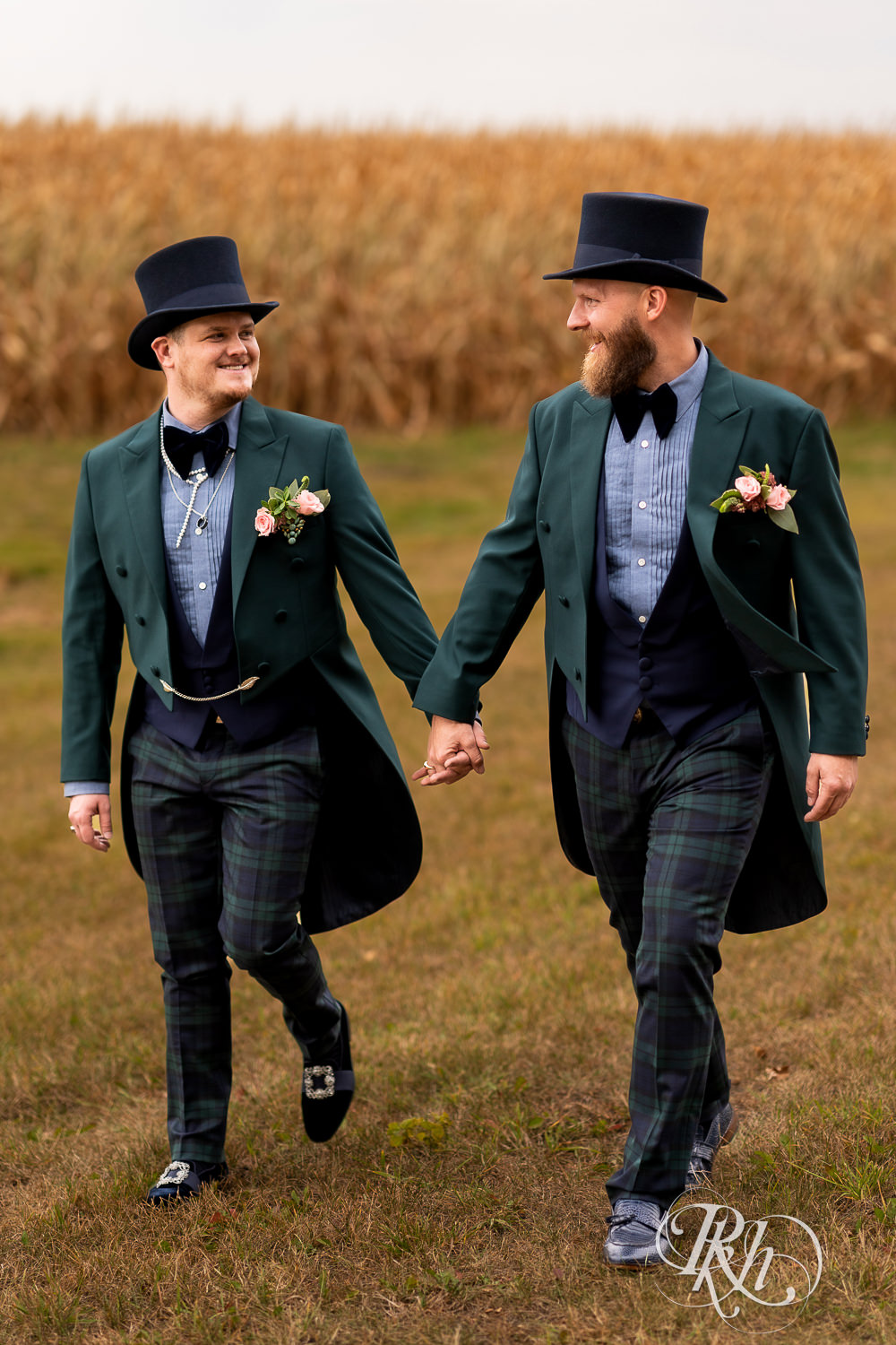 Grooms walking and holding hands in field on their wedding day.