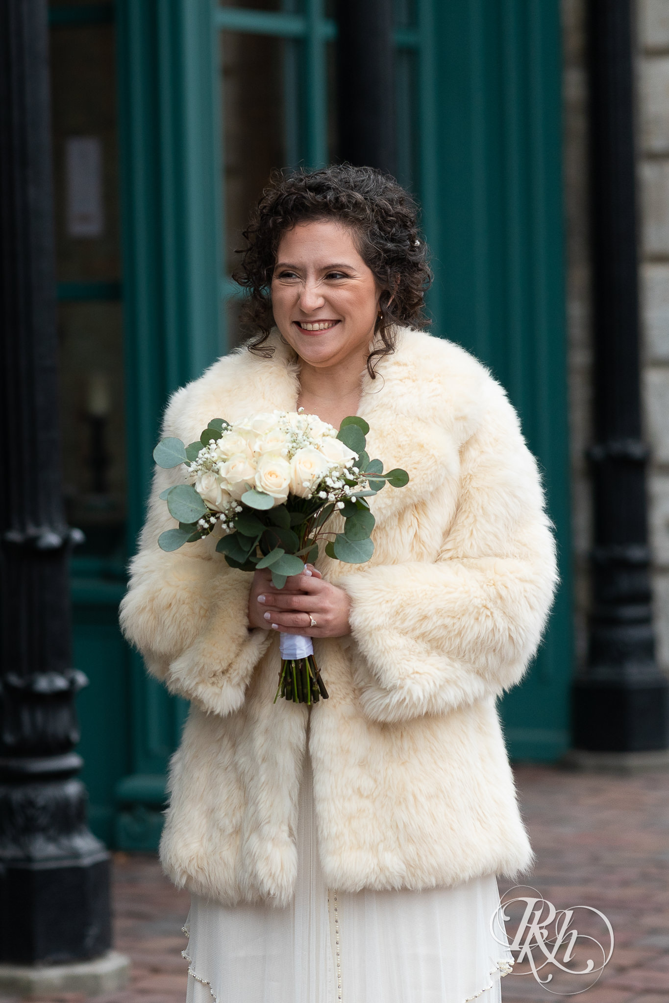 A bride holds a bouquet in her dress and fur coat in Saint Anthony Main, Minneapolis, Minnesota.